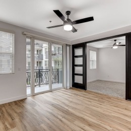 a living room with wood flooring ceiling fan sliding door to a balcony and a sliding door to a bedroom